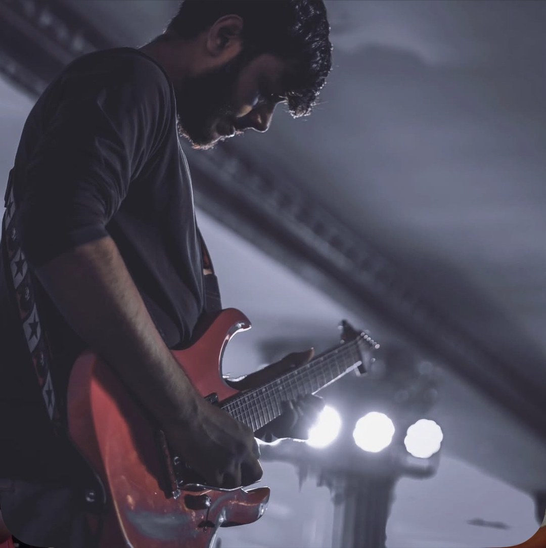 Arya Sen performing electric guitar under stage lights